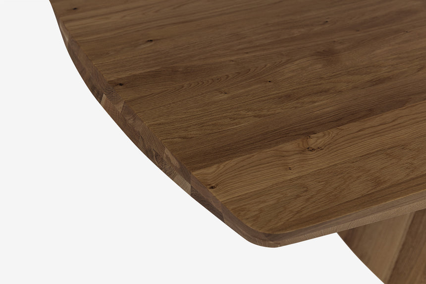 Zbliżenie zaokrąglonego brzegu drewnianego blatu i fragmentu podstawy.